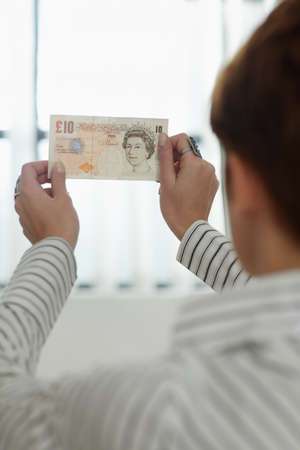 caucasian woman holding 10 pounds up to the light, examining watermarks. Vertical shape, rear view, copy spaceの写真素材