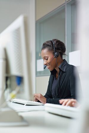 female african american customer service representative talking on the phone and typing on pc....