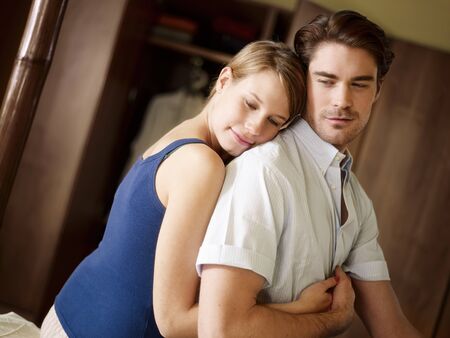 young husband and wife sitting on bed and hugging. Horizontal shape, waist up, side view