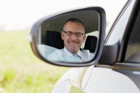mature caucasian business man looking at camera through rear view mirror. Horizontal shape, head and...