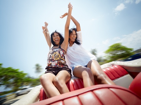 young adult brunette twin women sitting in convertible red car and laughing. Horizontal shape, front view, copy spaceの写真素材