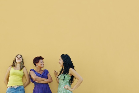 group of three female hispanic friends leaning on yellow wall and laughing. Horizontal shape, waist up, copy space の写真素材