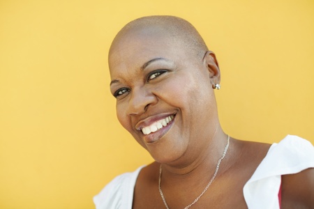 portrait of african 50 years old woman with bald head smiling at camera on yellow background. Head and shoulders, copy space の写真素材