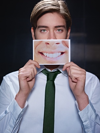 young business man holding photo of toothy smile on black background. Vertical shape, front view, waist upの写真素材