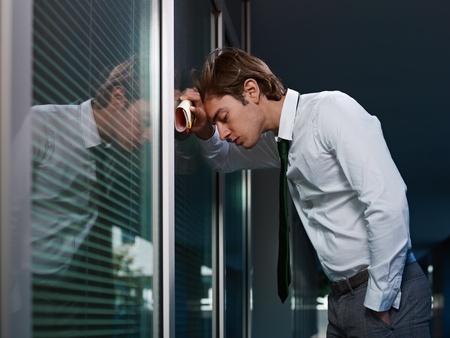 young adult italian business man banging his head against a window in office. Horizontal shape, copy spaceの写真素材