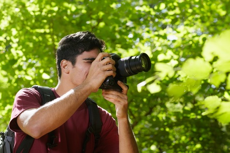 young hispanic man trekking among trees and taking pictures with dslr camera. Horizontal shape, side...