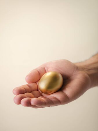 Man showing golden egg and holding it in hand. Concept of people securing savings, money, precious and valuable things, prizes. の写真素材