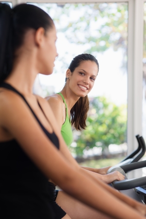 Young women talking and laughing while working out on exercise  bicycles in wellness clubの写真素材