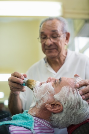 Elderly barber with shave brush applying cream to client in old style shopの写真素材