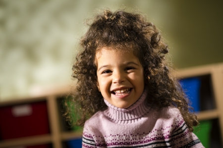 Portraits of children, happy 3 years old female with curly hair smiling and looking at camera in kindergartenの写真素材