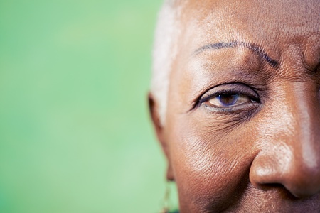 Old black woman portrait, close-up of eye and face on green background. Copy spaceの写真素材