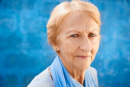Senior people portrait, happy old blonde woman in blu clothes smiling and looking at camera against blue wallの写真素材