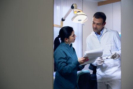 Dentist talking with female assistant in studio and looking at files. Copy space