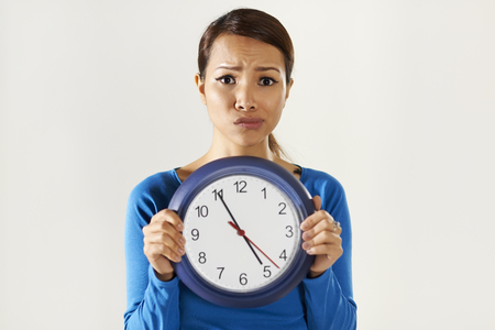 portrait of asian business woman holding big blue watch and looking at camera with worried...