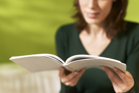 young caucasian woman reading book at home, sitting on sofaの写真素材