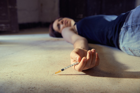 Closeup of young girl in heroine overdose holding syringe and lying on pavement. Copy spaceの写真素材