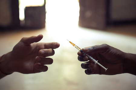 People abusing drugs, with African american man and caucasian guy sharing the same syringe to inject heroineの写真素材
