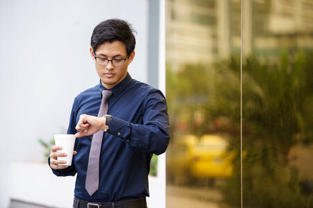 Portrait of chinese businessman standing near office building in Panama with coffee cup and checking...