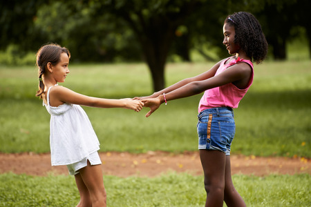 Two hispanic and african little girls playing ring around the rosie in public park and holding handsの写真素材