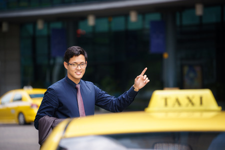 Asian business man standing near office buildings, calling yellow taxi and entering in carの写真素材