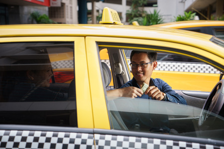 Asian man working as taxi driver in yellow car, with female client paying cash and leavingの写真素材