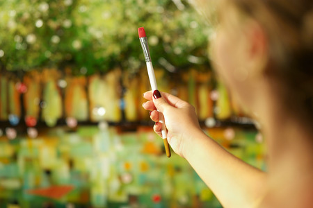 Rear view of woman hand holding painting brush and studying composition of picture on canvasの写真素材