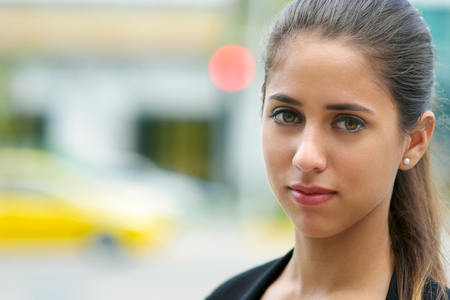 Portrait of young confident hispanic business person looking at camera and smiling in the street with cars passing behindの写真素材