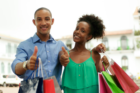 Portrait of black tourist heterosexual couple in Casco Antiguo - Panama City with shopping bags. The man and his girlfriend smile at the camera doing ok signの写真素材