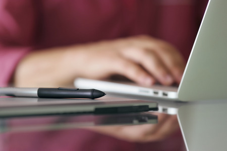 Photographer typing on keyboard of laptop computer. Closeup of digital tablet and stylus pen in foregroundの写真素材