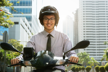 Young asian businessman commuting to job. The man rides a motorcycle scooter with white helmet and smiles at cameraの写真素材