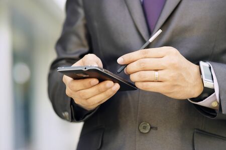 Closeup of businessman typing note on mobile phone. The man has a smartwatch and uses a digital pen...