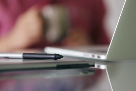 Photographer during coffee break while retouching image on laptop computer. Closeup of digital tablet and stylus pen. Copy space in foregroundの写真素材