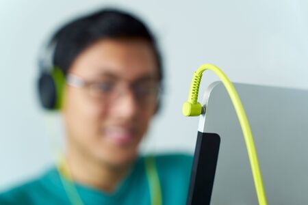 Chinese man relaxes on sofa and watches podcast on tablet pc, listening with green big earphones. Narrow focus on jackの写真素材