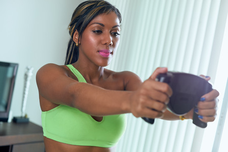 Young adult african american woman in sports clothing measuring body fat with electronic tool. The girl holds the sensors with her hands and looks at the displayの写真素材