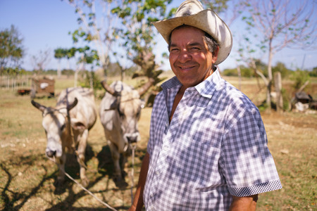 Farming and cultivations in Latin America. Portrait of middle aged hispanic farmer sitting proud in his tractor at sunset, holding the volante. He looks at the camera and smiles happy.の写真素材