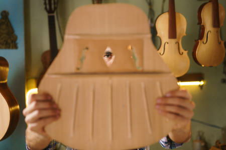 Lute maker shop and acoustic music instruments: young adult artisan carving and chiseling the body of a classic guitar. He is examining the design of the holes in the wooden body.の写真素材