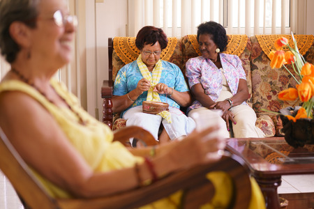 Old people in geriatric hospice: Senior woman sitting on sofa in hospital, knitting with ball of wool between other ladies. The aged grandma is pensive and focused on her hobby.の写真素材