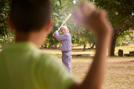 Grandparents spending time with grandson: Senior man playing baseball with his grandson in park. The...