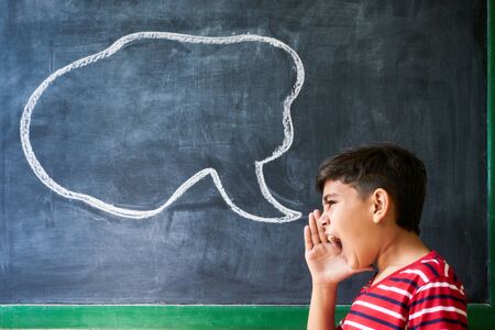 Concept on blackboard at school. Young people, student and pupil in classroom. Hispanic boy screaming in class with drawing of cloud on blackboard. Portrait of frustrated male childの写真素材