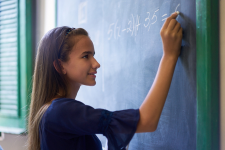Young people and education. Group of hispanic students in class at school during lesson. Portrait of happy girl doing math exercise at blackboardの写真素材