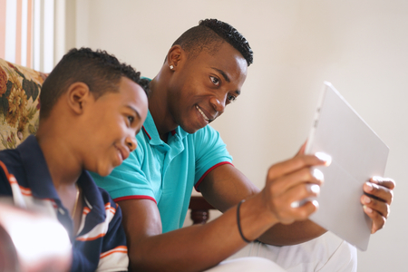 Happy black family at home. African american father and child playing game with tablet. Dad and son having fun with laptop computerの写真素材