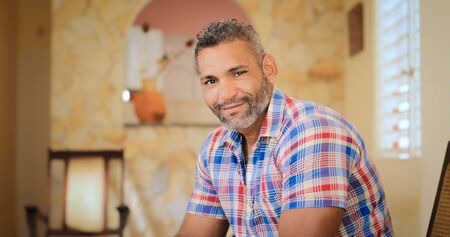 Portrait of homosexual adult man. Happy hispanic gay smiling at camera, sitting on sofa at home.