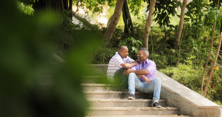 Homosexual couple, gay people, multiethnic lgbt relationship. Two happy male partners meeting in park, hugging themselves and smiling.の写真素材