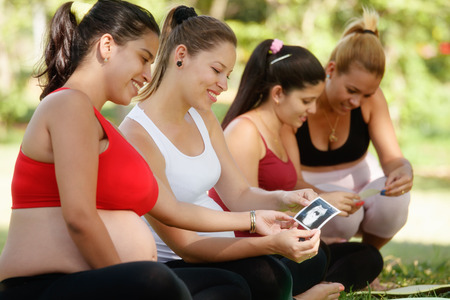 Pregnant women, group of mothers during pregnancy. Lesson in city park with happy female friends smiling and looking at ecography scans.の写真素材