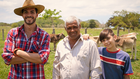 Everyday life for farmers with cows in the countryside. Peasants work in Latin America with livestock in family country ranch. Portrait of happy grandfather, dad and child smiling.の写真素材