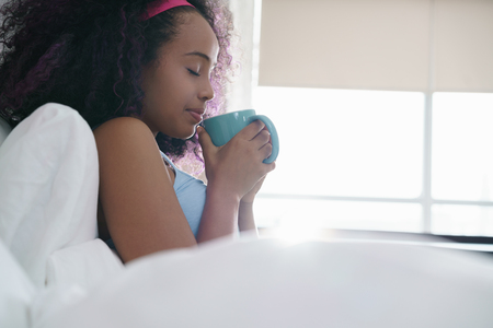 Black Woman Drinking Coffee In Bed Smilingの写真素材