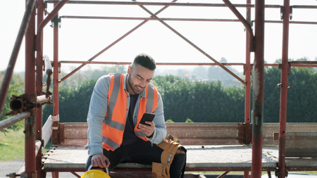 Man Working In Construction Site Smiling And Using Smartphoneの写真素材