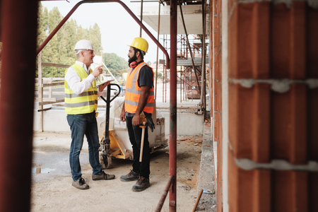 Portrait Of Happy Construction Site Supervisor Talking To Manual Workerの写真素材