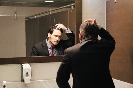 Worried Hispanic Business Man Looking At Hairline In Office Restroomsの写真素材