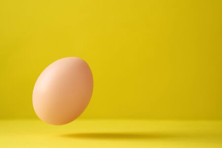 Chicken Egg Falling On Ground Against Yellow Backgroundの写真素材